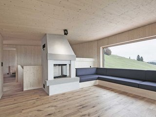 Zimmermannshandwerk trifft auf detailreiche Architektur: Im Dachgeschoss schliesst die eingebaute Sitzbank an das Cheminée an. Dreischichtplatten in Sichtqualität tragen zur gemütlichen Atmosphäre bei. Ein grosses Fenster rahmt den Blick in die Landschaft.
