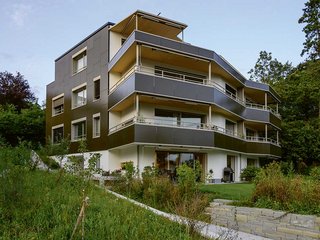 In Höngg (ZH) hat das Architekturbüro Kämpfen Zinke + Partner ein wegweisendes Mehrfamilienhaus realisiert (Schweizer Solarpreis 2019, Diplom Norman Foster Award 2019): PV-Zellen auf dem Dach und rings ums Haus machen den Holzbau zu einem 126-Prozent-Plusenergiehaus. Die Fassade des gesamten Gebäudes – auch die Balkonschicht, die zugleich als konstruktiver Sonnenschutz dient – ist mit PV-Modulen eingekleidet. Aus der Distanz betrachtet, erscheint die solaraktive Fassade in einer einheitlichen Farbe. Tatsächlich aber handelt es sich um ein aufgedrucktes Karomuster, bei dem zugunsten einer optimalen Energieausbeute nur jedes zweite Quadrat schwarz ist. Durch diesen gestalterischen Kniff sinkt der Effizienzgrad der Module um etwa 18 Prozent, was die Architekten als tolerierbar erachten.