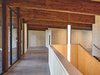 Im Inneren trifft kühler Sichthartbeton am Boden auf warme Dreischichtplatten an Wand und Decke sowie Balken und Stützen aus Fichte/Tanne.  
