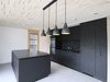 Auch die Küche mit schwarzen OSB-Fronten stammt von der Alpiger Holzbau AG. Die zehn Zentimeter abgehängte Decke aus Dreischichtplatten ist mit einer dekorativen Akustikfräsung versehen. 
